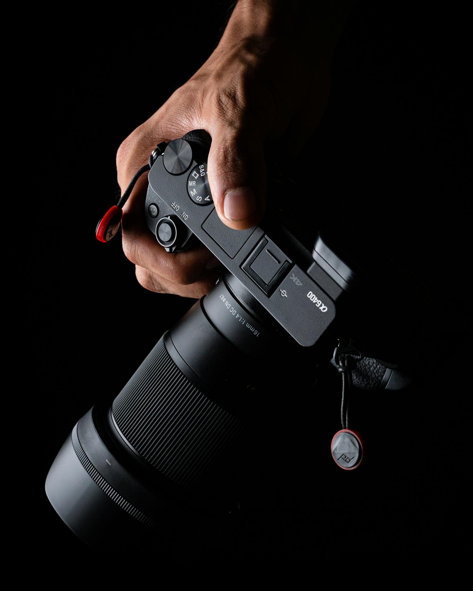 From above anonymous person holding modern professional photo camera with lens on black background